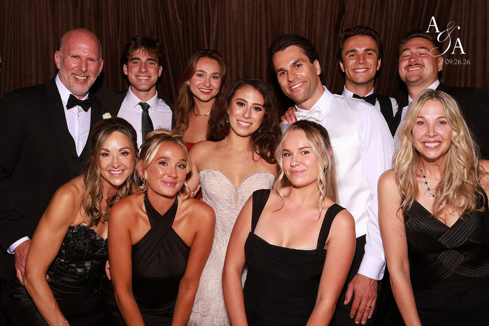 Alyssa and Alex in the middle of nine family and friends in black tie, everyone smiling at the camera at Alyssa + Alex