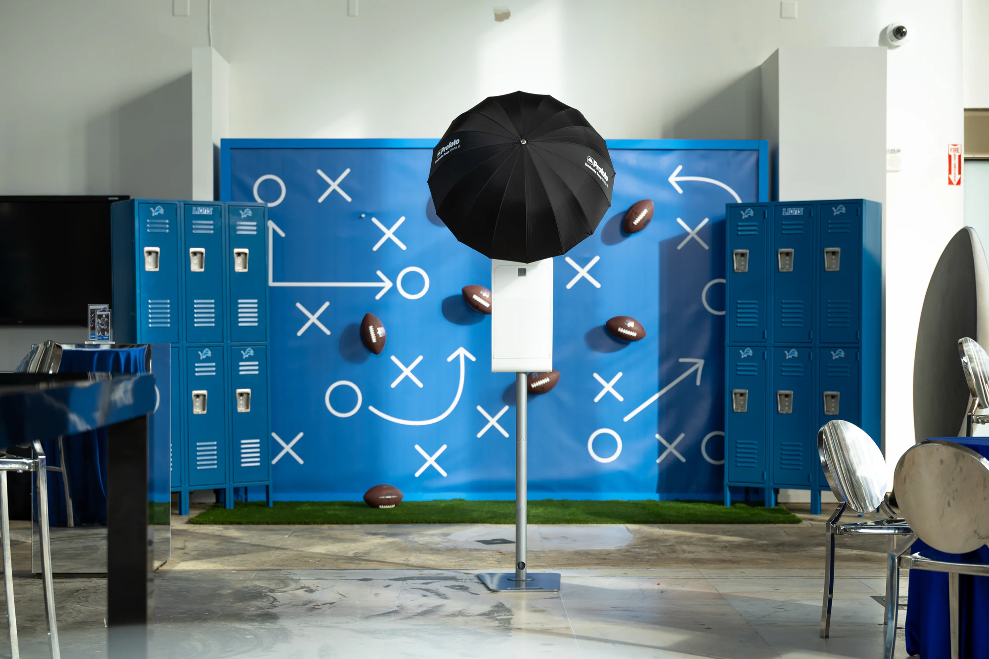 The Portrait Booth lit by a black umbrella in front of a blue playbook wall of chalk X's, O's and footballs, between Lions lockers