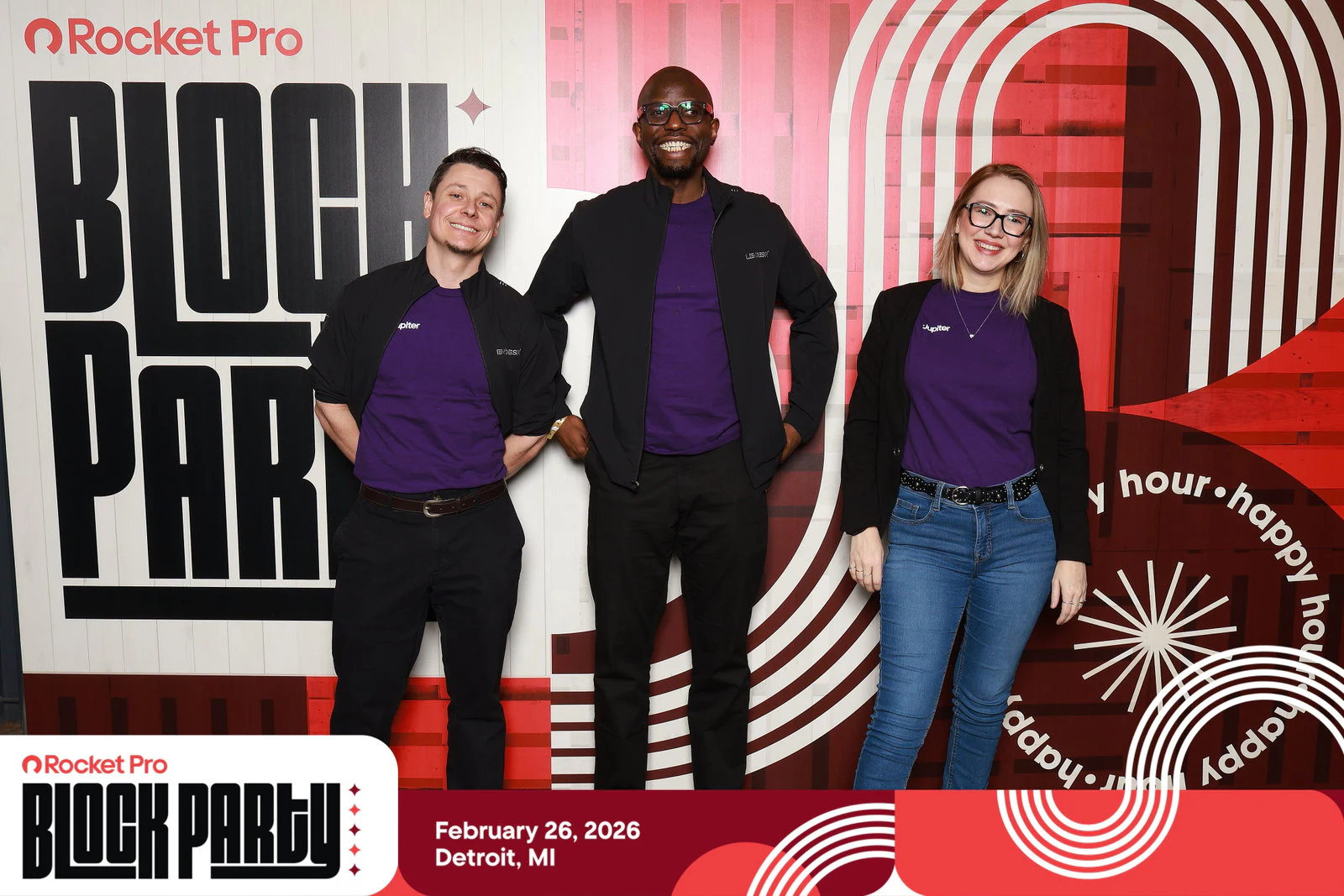 Three people in matching purple shirts and dark jackets standing in front of the Block Party printed wall at Rocket Pro Block Party