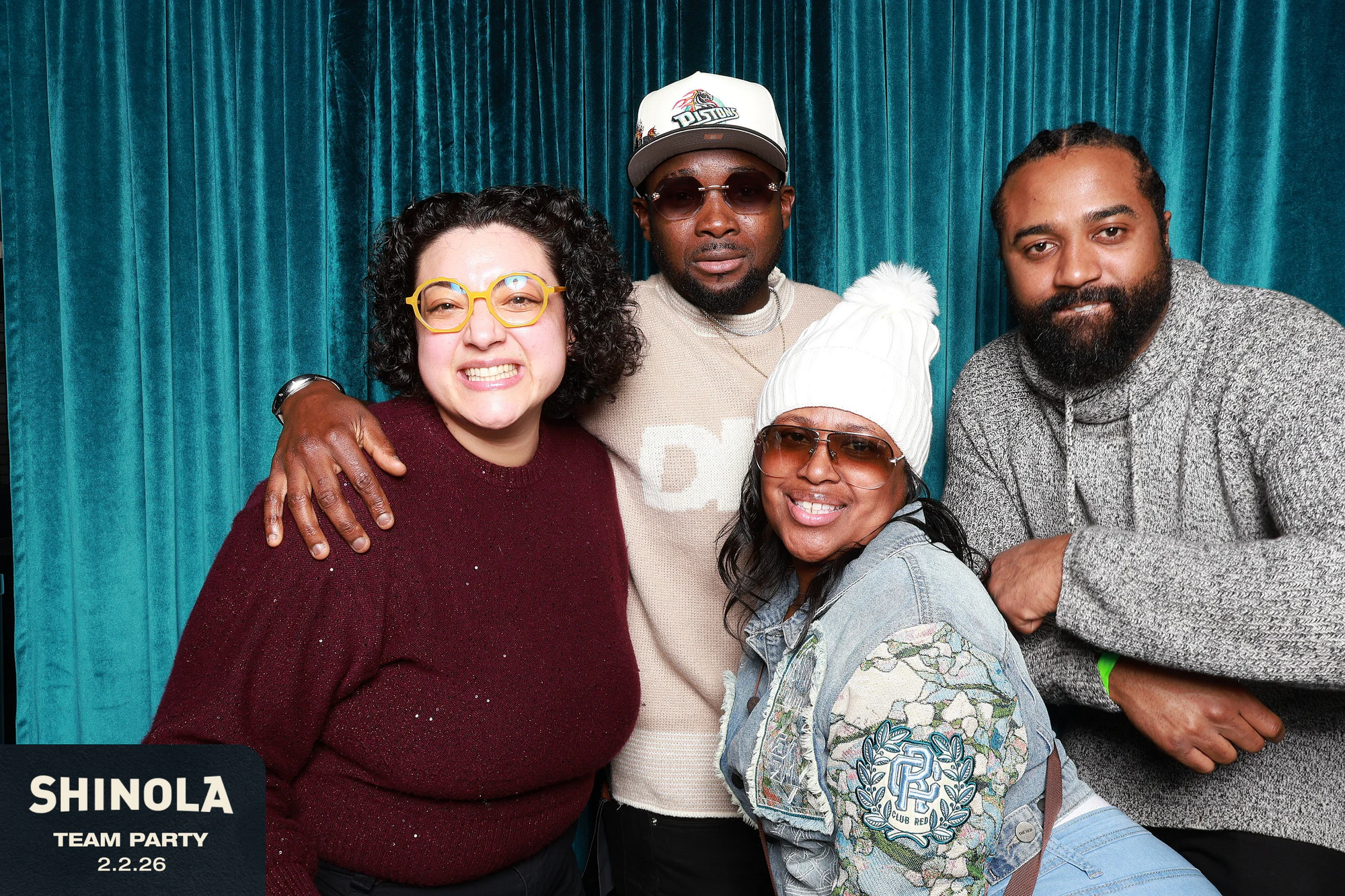 Four coworkers, arms around each other, in front of the teal velvet at Shinola Hotel Team Party