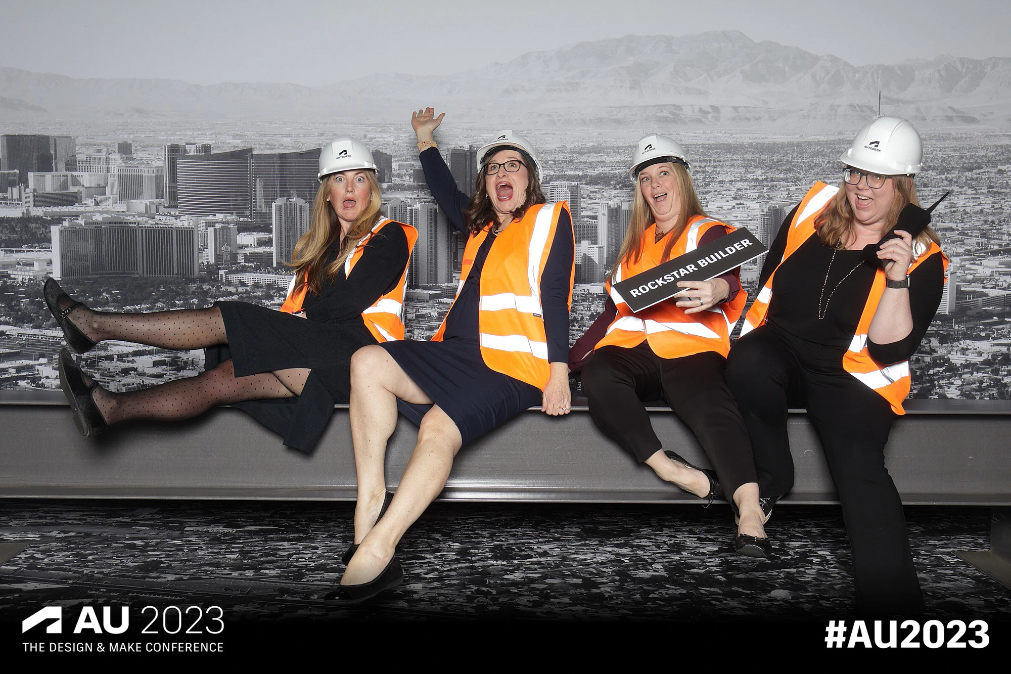 Four women on the girder mid-shout, one holding a ROCKSTAR BUILDER sign